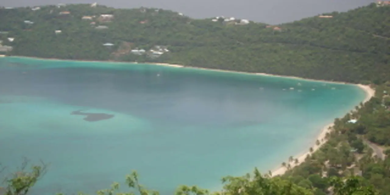 Magens Bay from above: a long curve of white sand and pale turquoise water between two green, wooded headlands