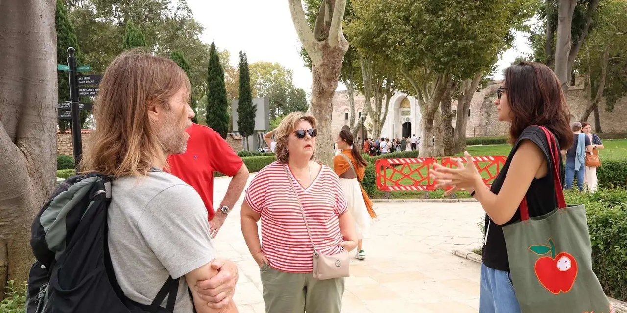 A guide talking to a small group of visitors in a sunny palace courtyard