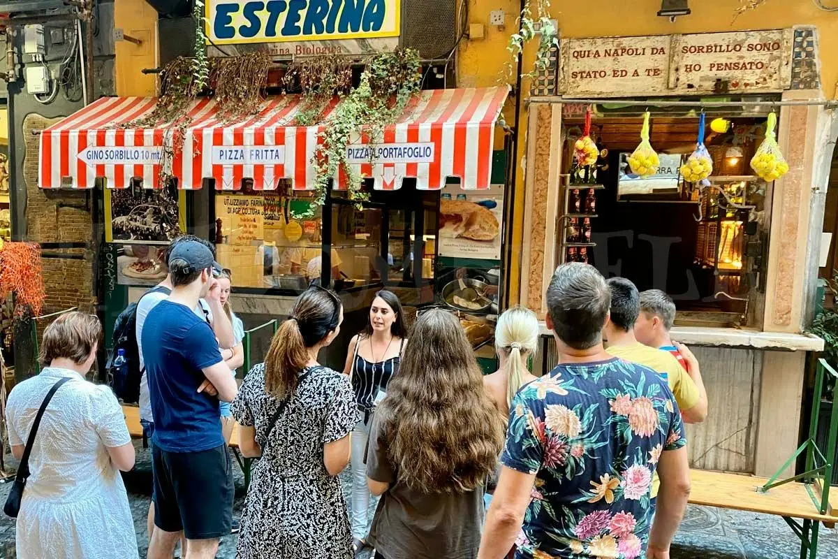 A small group gathered outside a fried-pizza shop with red-and-white striped awnings