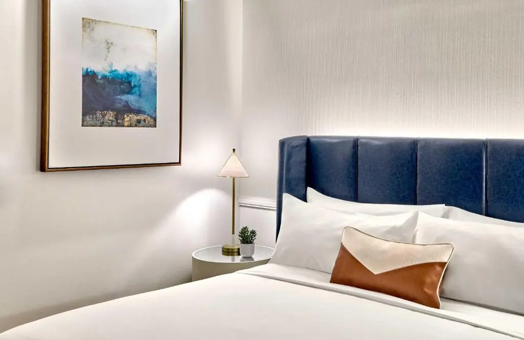 A bed with a blue leather headboard, white linens and a framed blue abstract print in an Omni Fort Lauderdale Hotel room