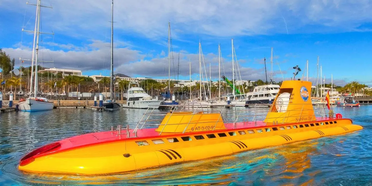 A yellow tourist submarine moored in a marina full of white yachts