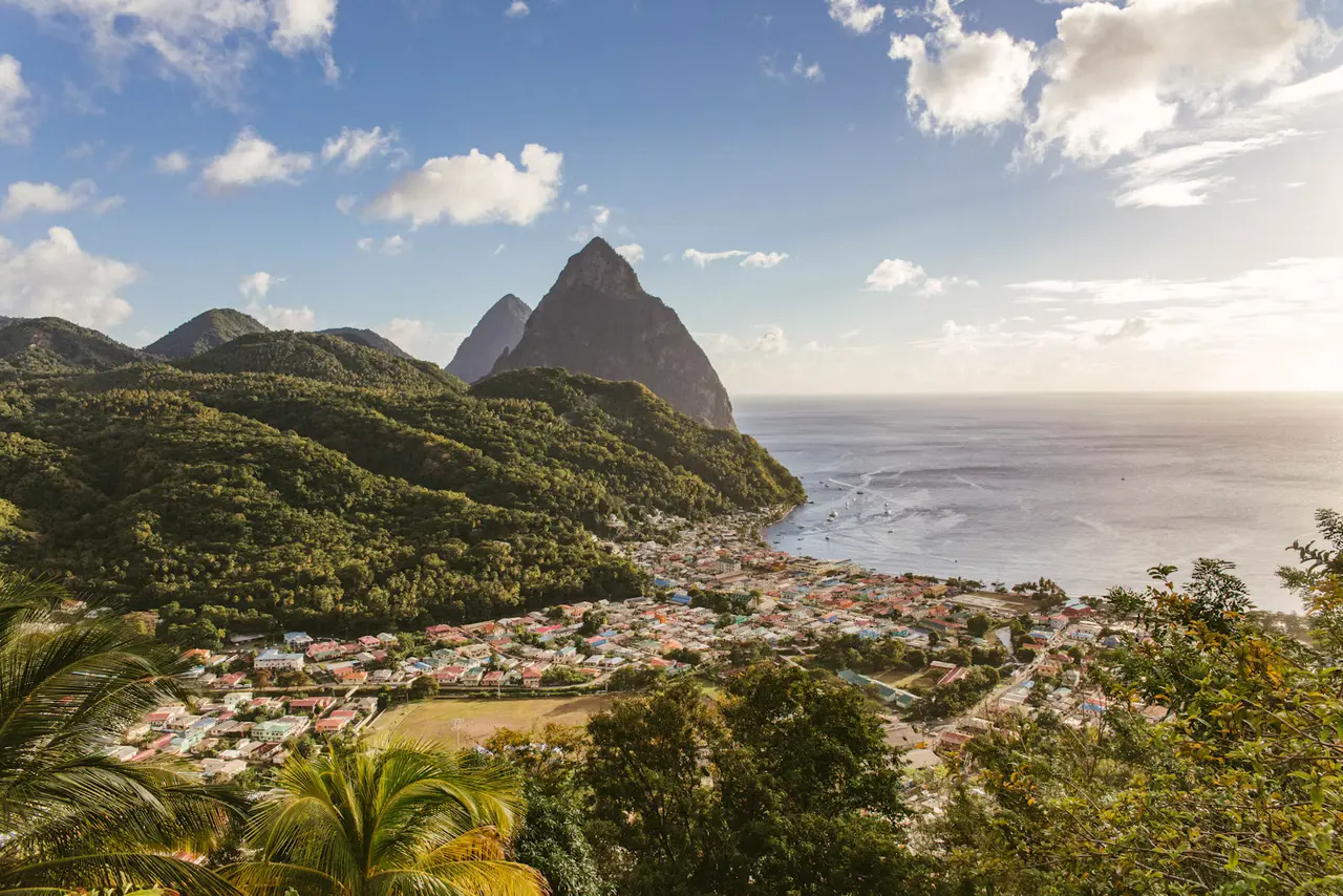 The Pitons, two steep green volcanic peaks, rising above a pastel-roofed town and the blue sea in Soufrière, St. Lucia, about 20 miles south of Castries