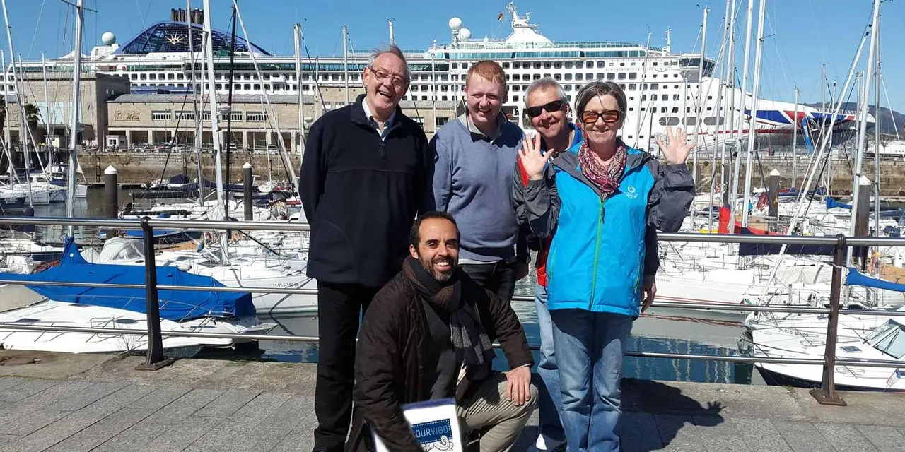A guide crouching in front of a small, smiling group at a marina, with a cruise ship docked behind them