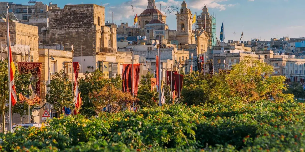 A sunny view over the Three Cities' rooftops and church domes, framed by flags