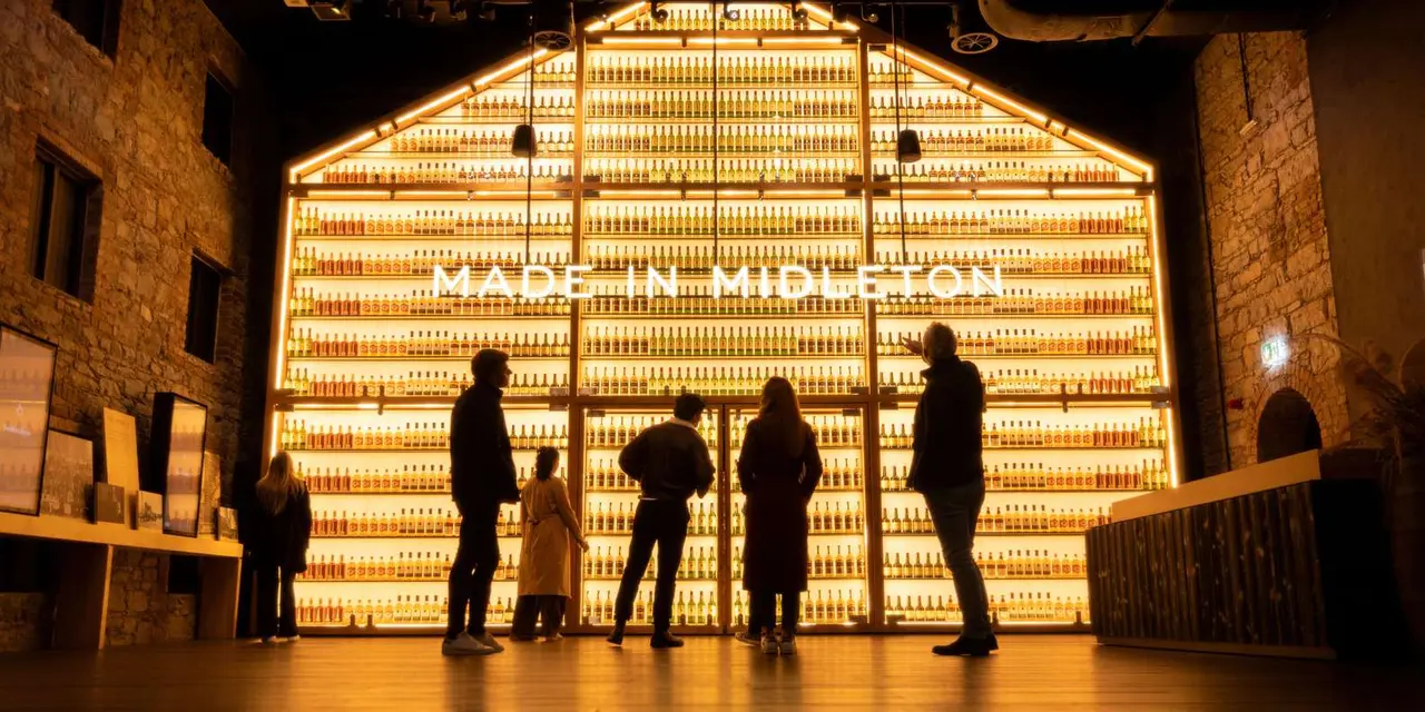 Silhouetted visitors in front of a glowing wall of whiskey casks lettered 'Made in Midleton'