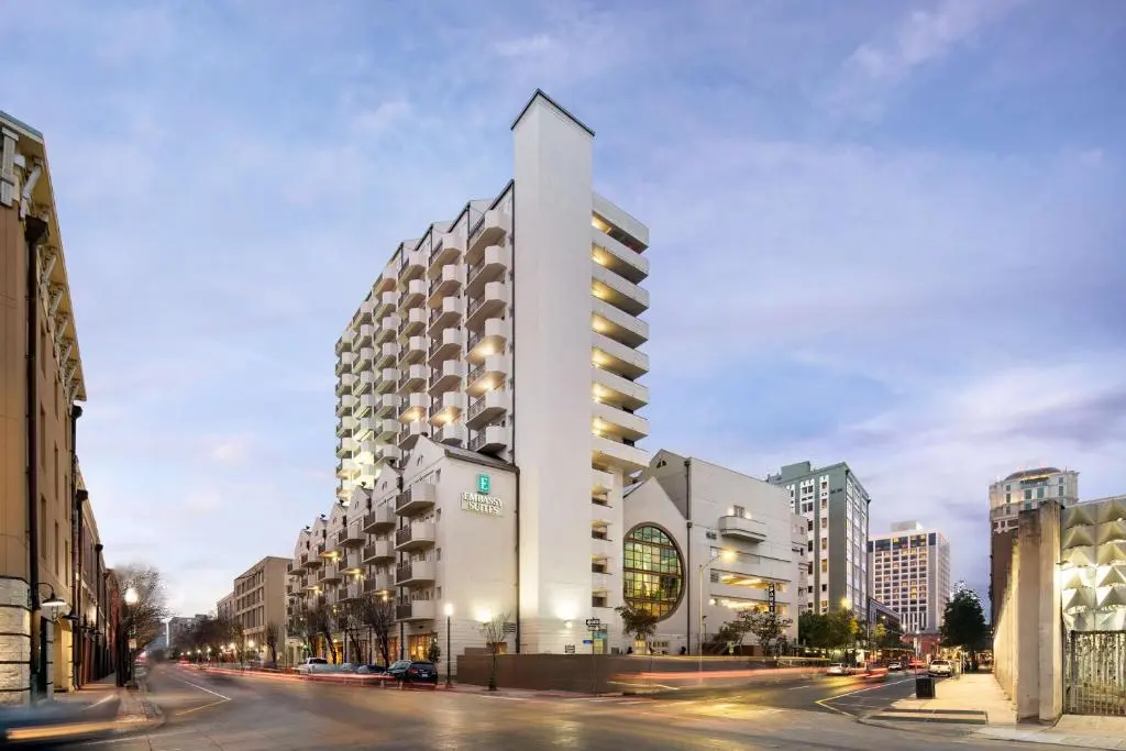 The white Embassy Suites tower on Julia Street at dusk, with balconies stepping up its side and lit windows