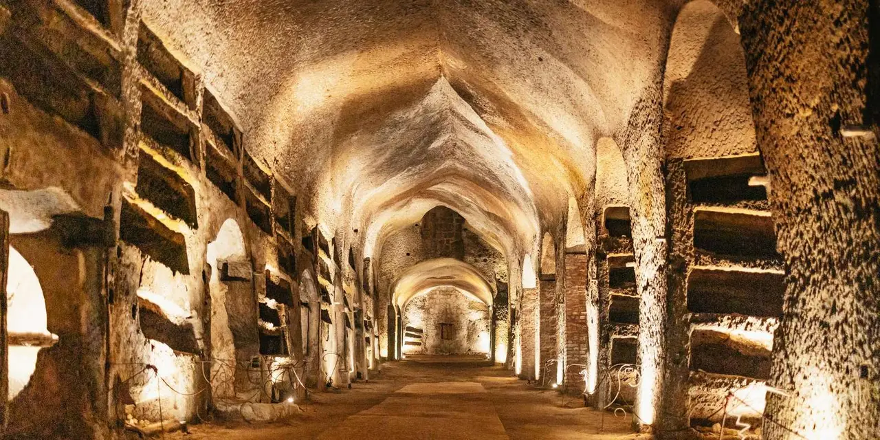A long vaulted tunnel cut from golden rock, lined with burial niches