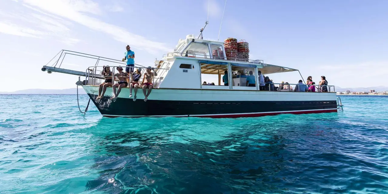 A white and green traditional boat full of passengers on clear turquoise water