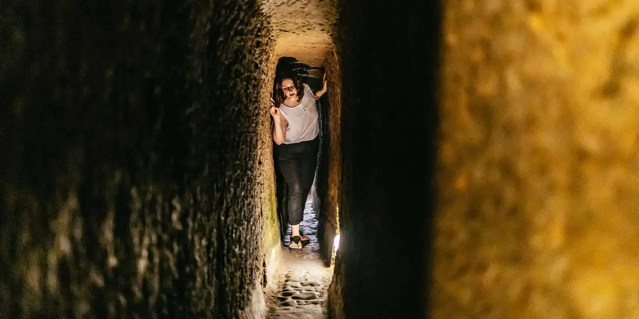 A visitor squeezing sideways through a narrow, lit rock passage underground