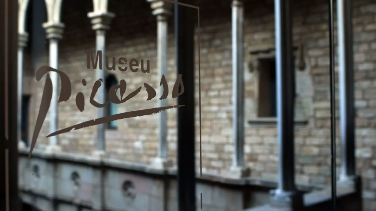 The Museu Picasso lettering etched on a glass door, with the stone arches of an old courtyard behind