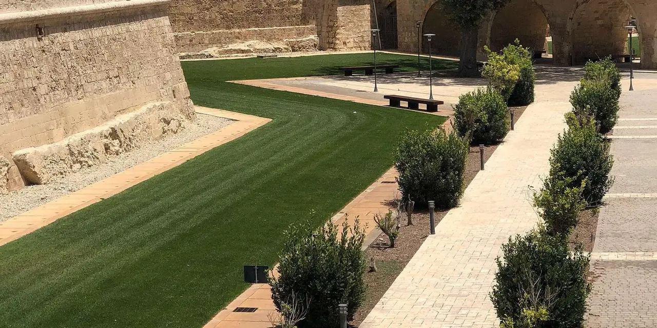 Mdina's honey-stone bastion walls rising above a landscaped garden in the old moat