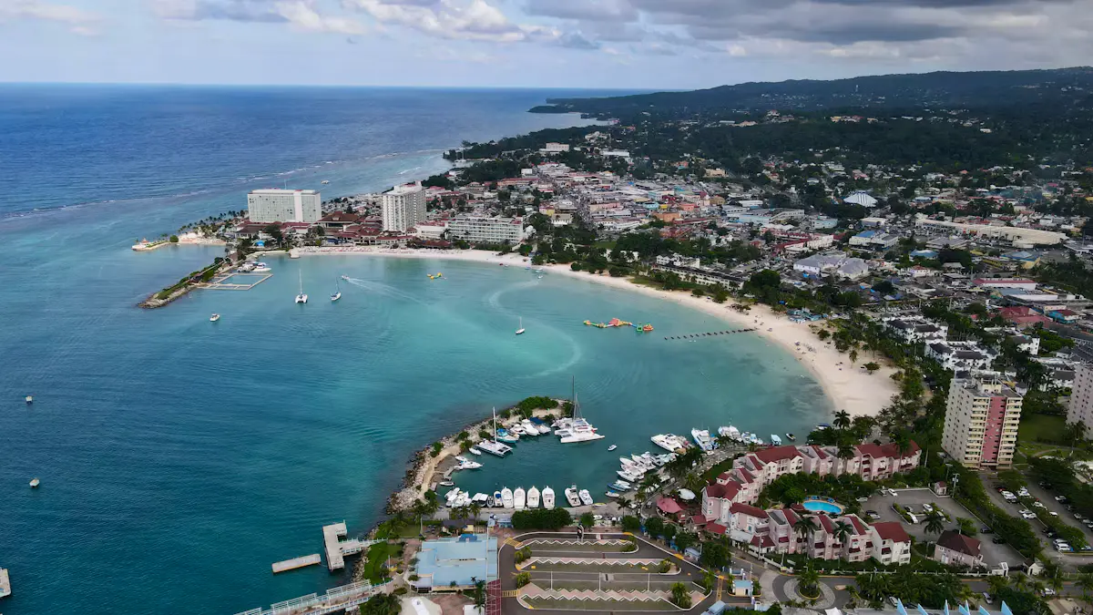 Aerial view of the curved sandy bay at Ocho Rios, Jamaica, with the marina and harbour in front, hotels along the shore and green hills behind the town