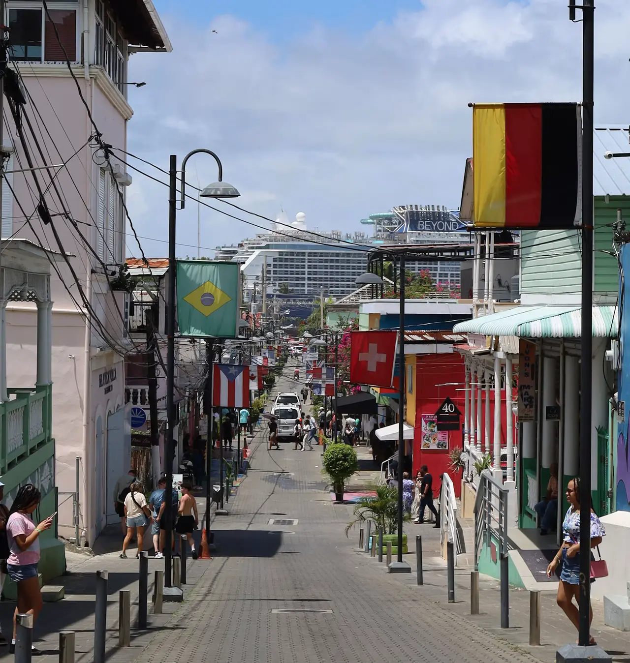 A colourful street in Puerto Plata's old town lined with pastel wooden buildings and national flags, with a docked cruise ship rising at the end of the street