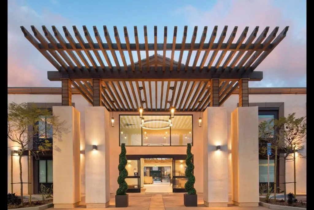The Cove Hotel's entrance at dusk, with a wooden pergola over the doorway and spiral topiary in planters