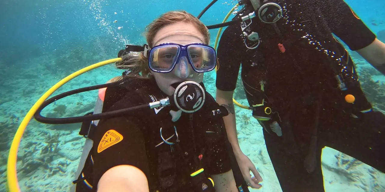 A smiling woman in mask and regulator beside a diving instructor, underwater