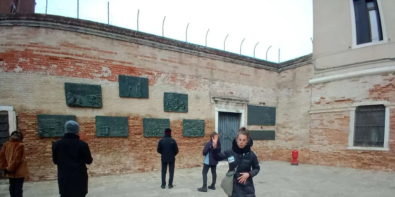 People in the Campo del Ghetto Novo in front of a brick wall hung with bronze memorial plaques
