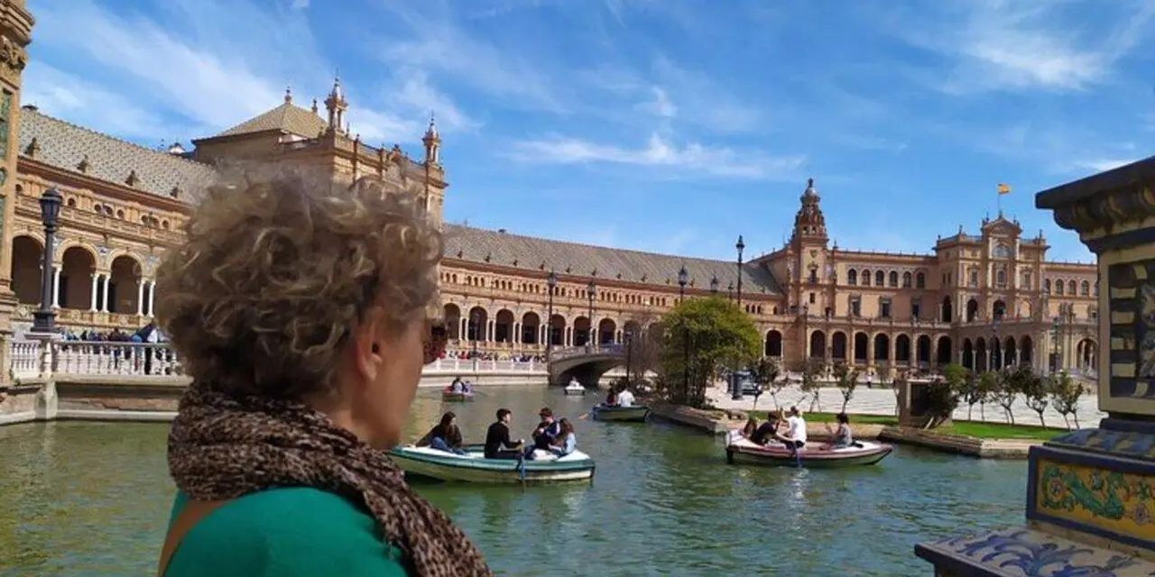 Seville's Plaza de España, with its curved brick-and-tile palace, a canal with rowboats and a visitor looking out over it