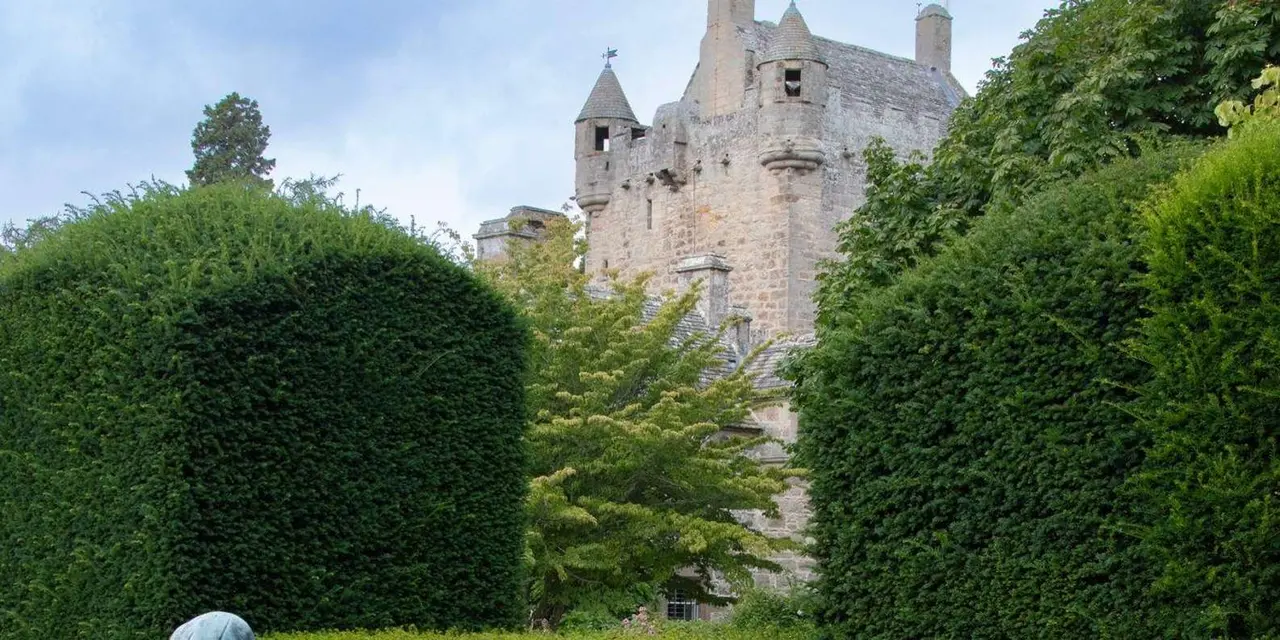 Cawdor Castle's turreted stone tower rising behind clipped yew hedges under a pale sky