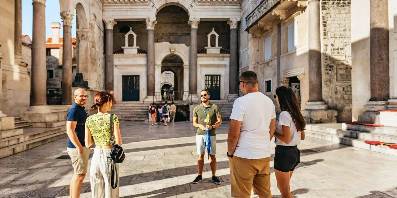 A guide talking to two visitors in the Peristyle of Diocletian's Palace, with stone columns and arches behind