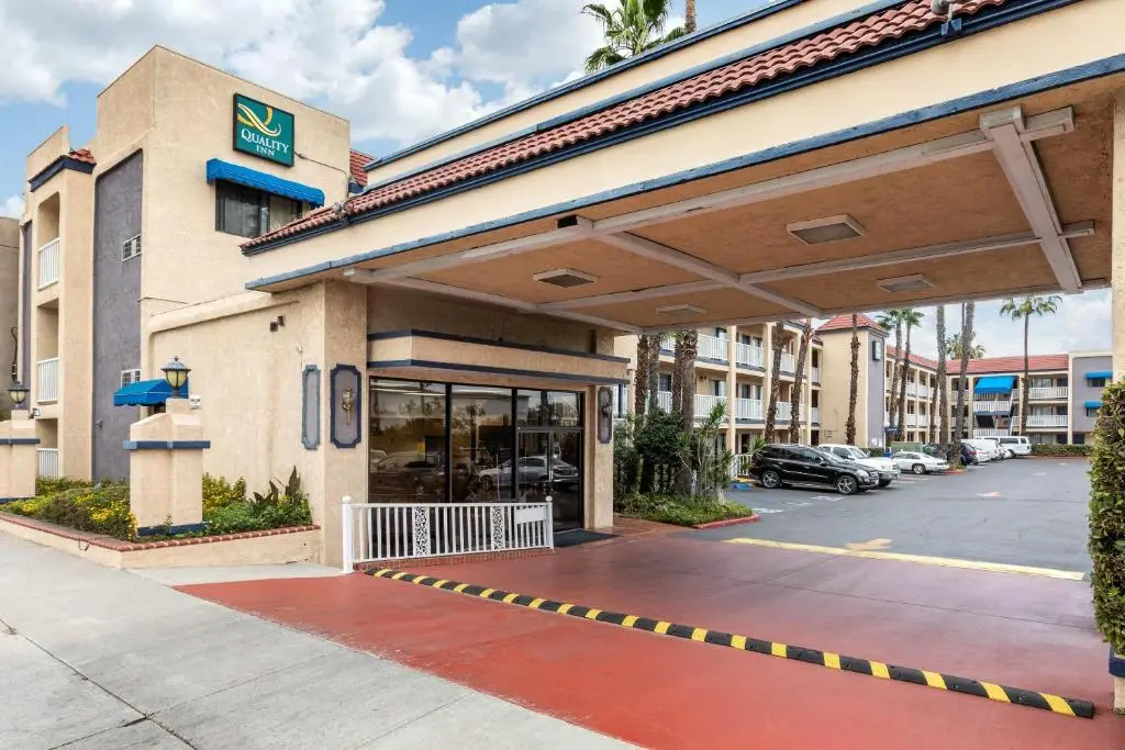 The covered drive-up entrance of the Quality Inn - Torrance Lomita, a tan building with a red tile roof and palm trees