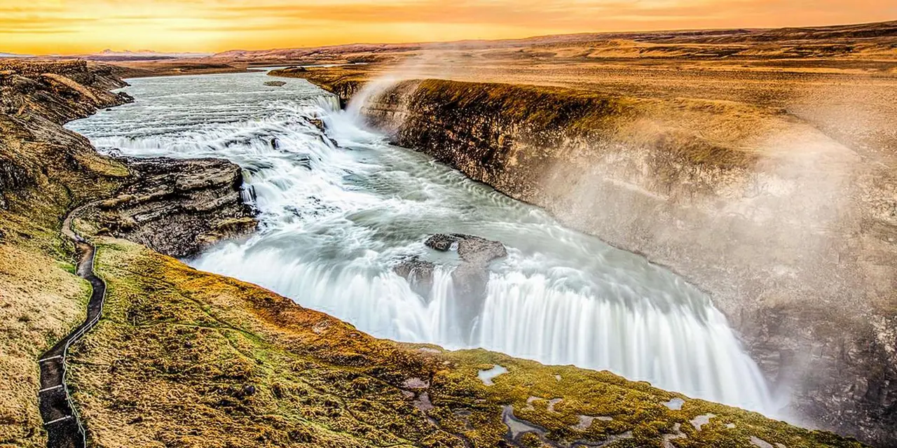 Gullfoss waterfall pouring into its gorge under an orange sunrise or sunset sky