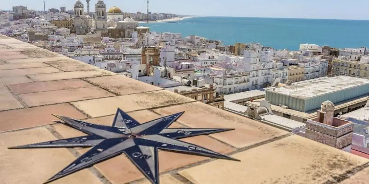 A compass rose inlaid in a paved rooftop terrace, with the white rooftops of Cádiz and the sea stretching beyond