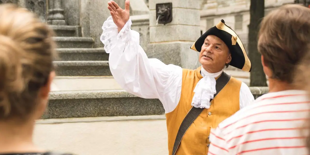 A guide in a tricorn hat and colonial costume gesturing to a tour group