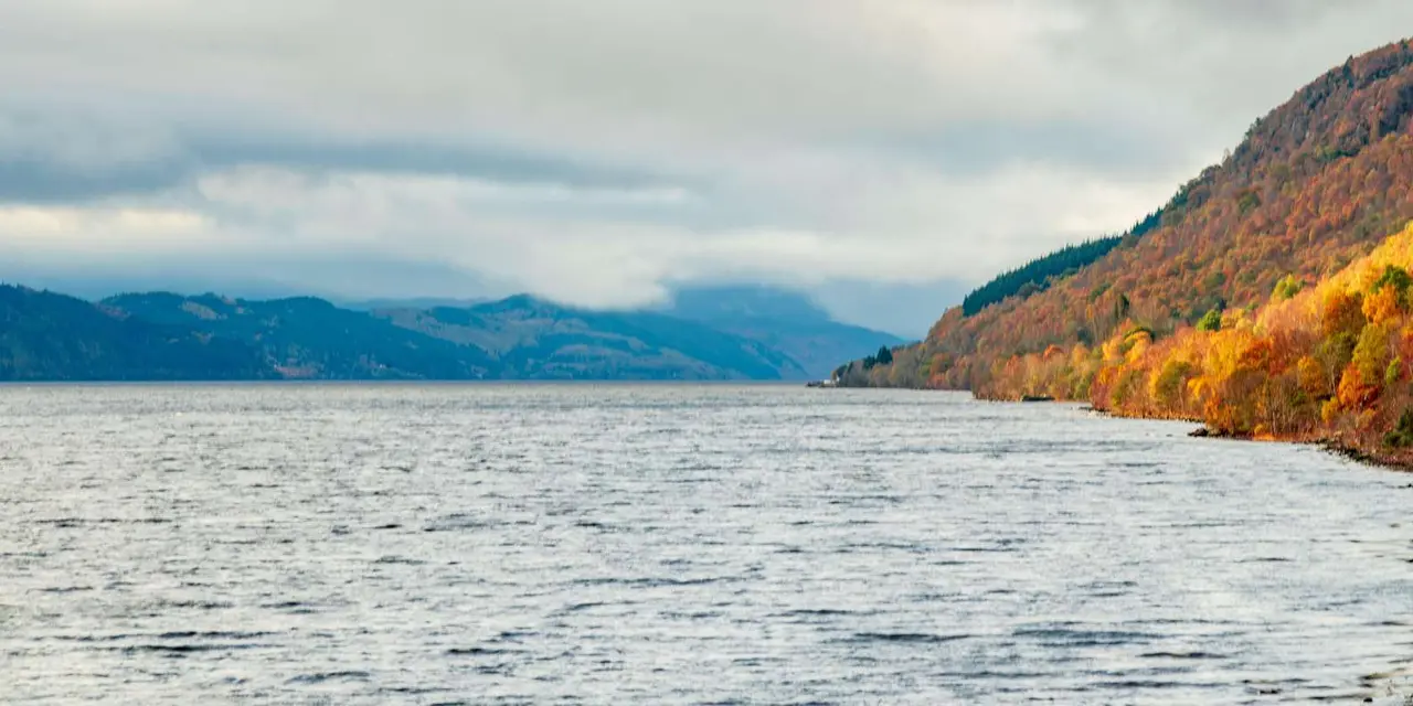 Loch Ness under heavy cloud, with autumn-coloured hillsides sloping to the water on the right