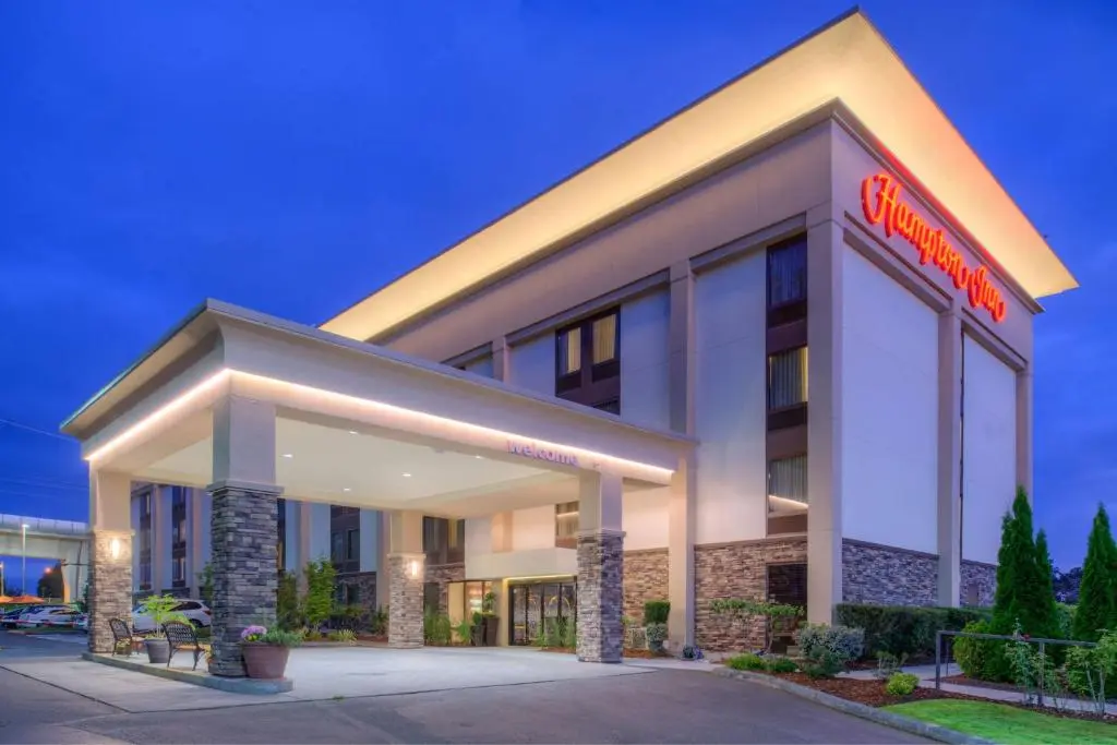 The Hampton Inn Seattle Airport's lit entrance canopy and stone columns against a deep blue evening sky
