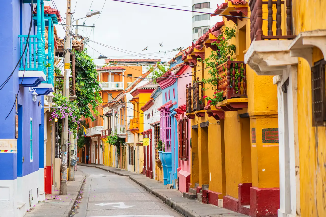 A narrow street in Cartagena lined with blue, pink and yellow colonial houses with wooden balconies and hanging plants