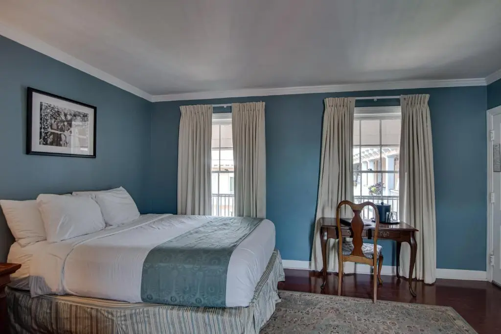 A Malaga Inn guest room with blue walls, a white bed and tall windows with cream curtains