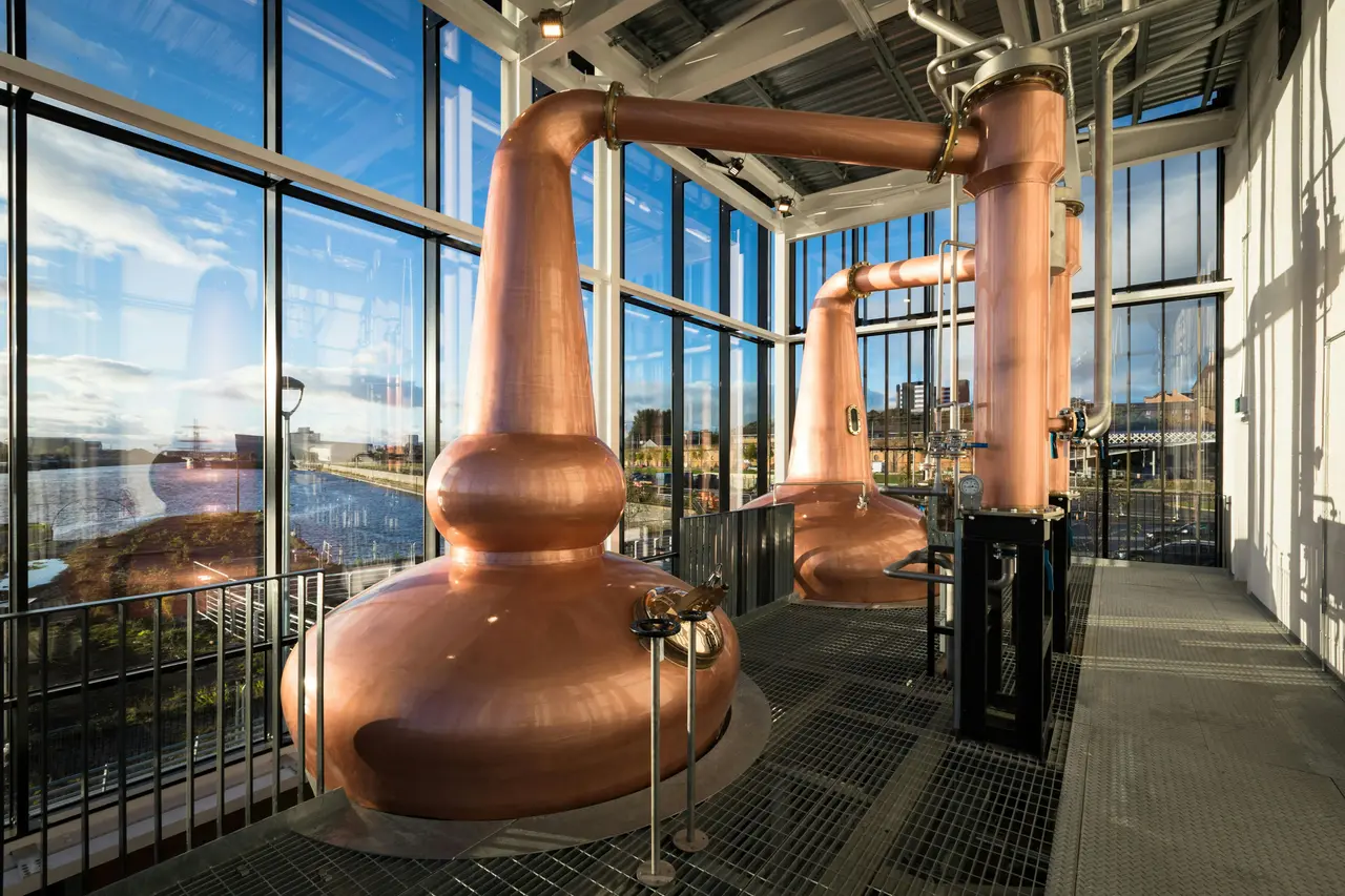 Two tall copper stills beside floor-to-ceiling windows looking out over the river