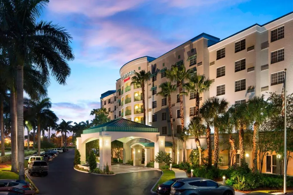 The Courtyard by Marriott Fort Lauderdale Airport & Cruise Port at dusk, a curved building with a green-roofed entrance and palm trees