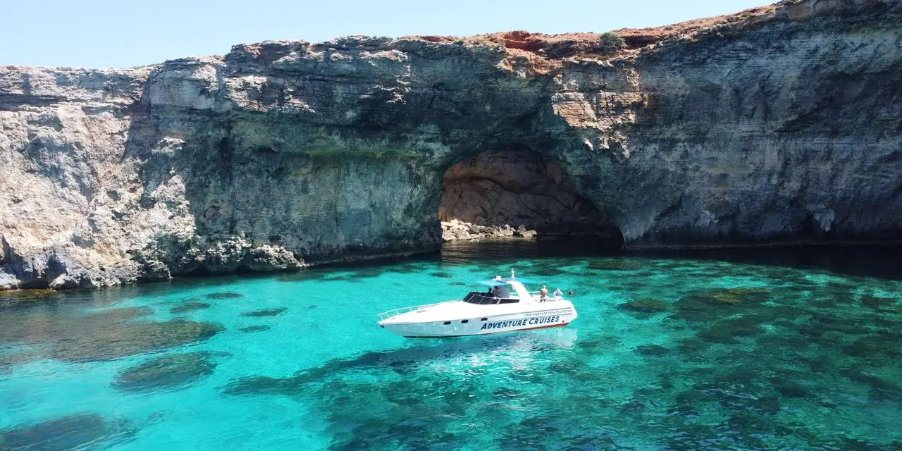 Turquoise water at the foot of Comino's pale limestone cliffs, with a white boat moored in the lagoon