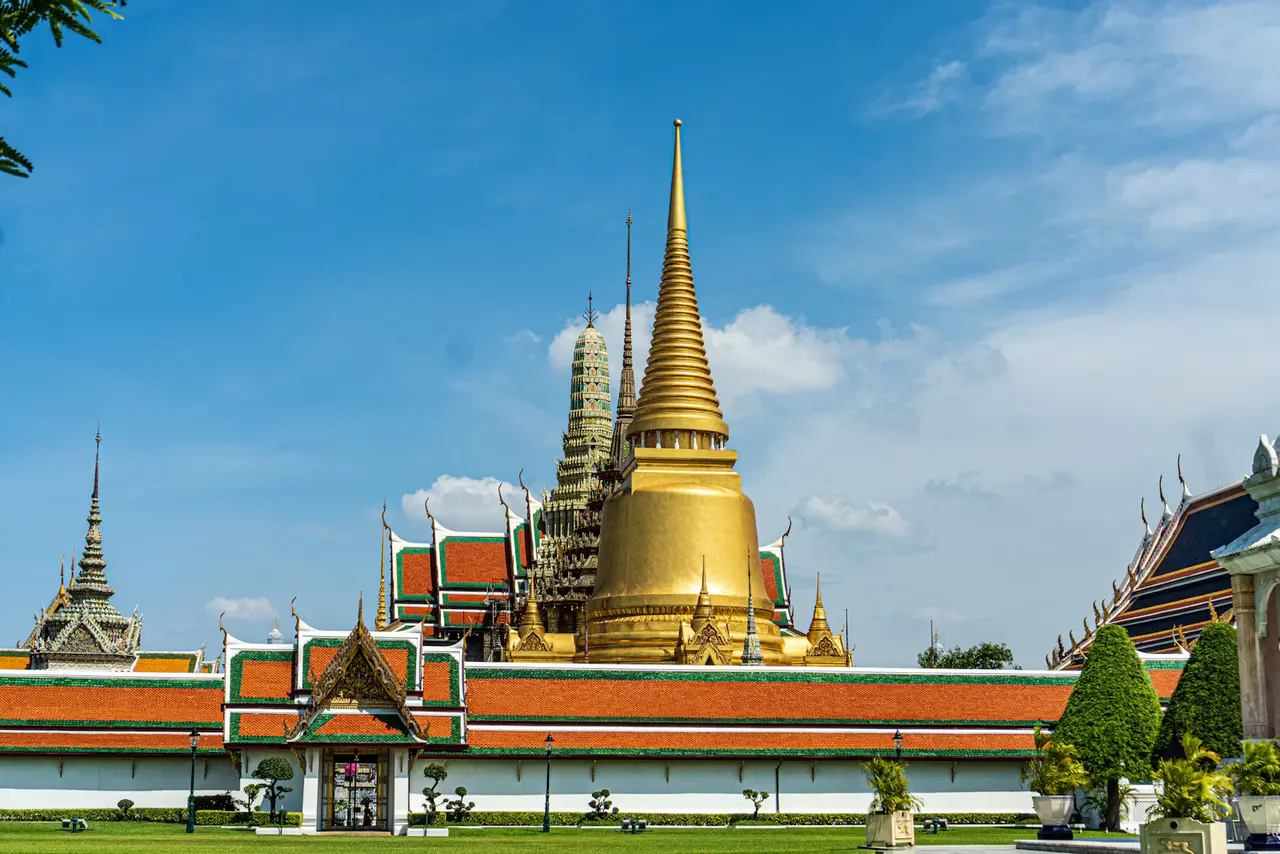 The golden chedi and red-and-gold roofs of Wat Phra Kaew at Bangkok's Grand Palace under a bright blue sky, about two hours by road from Laem Chabang