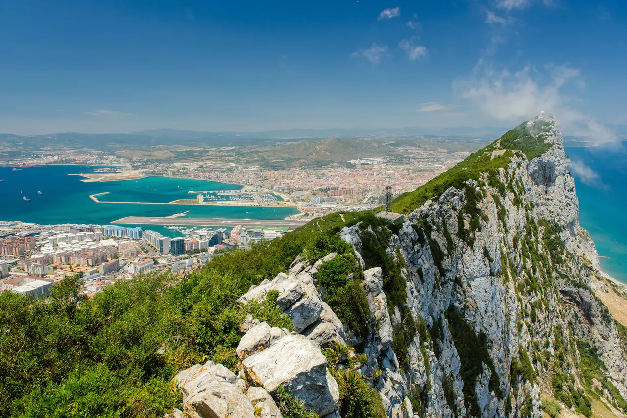 The limestone ridge of the Rock of Gibraltar dropping to turquoise water, with the town, the harbour and the airport runway spread out below