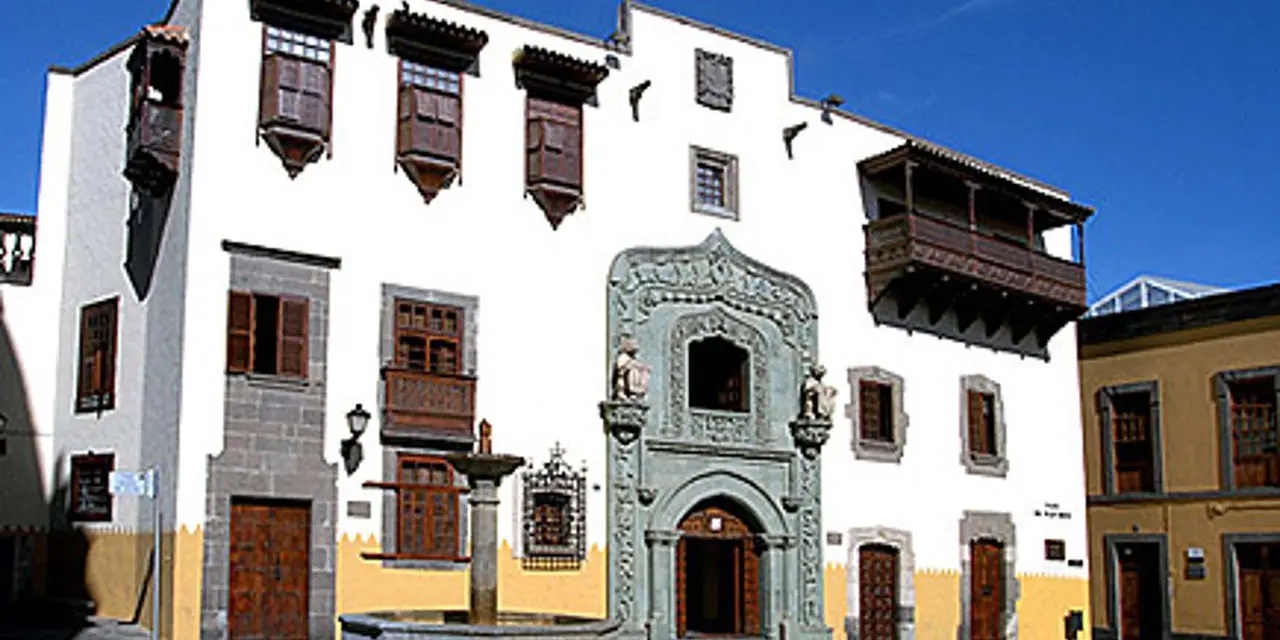 A whitewashed colonial house with a carved stone doorway and wooden balconies under a blue sky