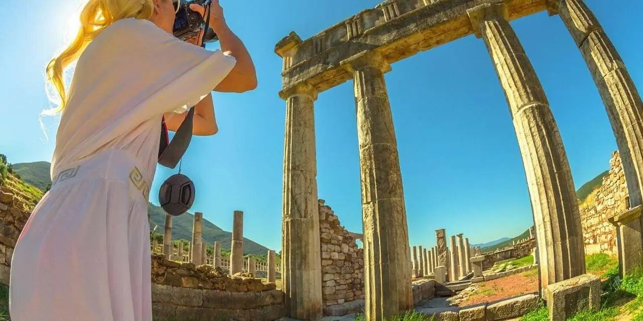 A woman in a sun hat photographing ancient stone columns in bright sunshine