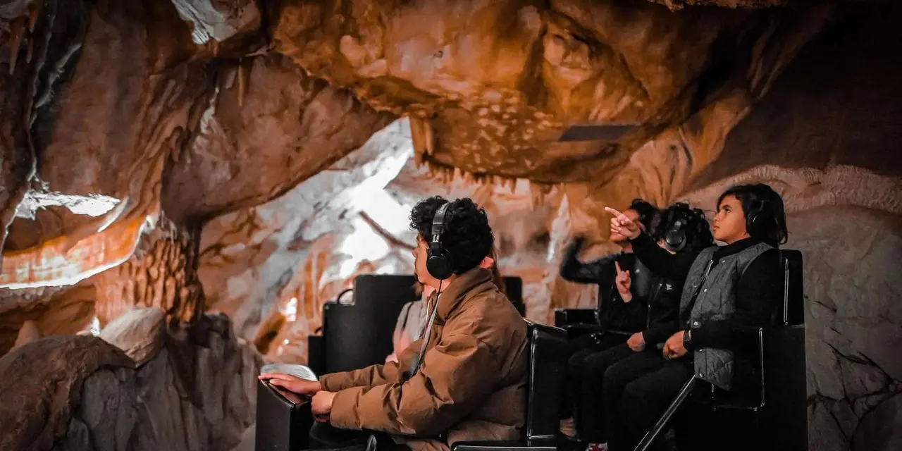 Visitors seated in a ride vehicle passing painted rock walls inside the recreated Cosquer cave