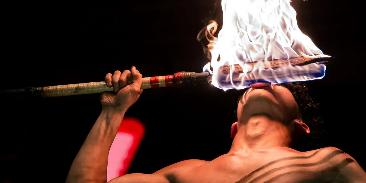 A fire knife dancer leaning back under a burst of flame at night