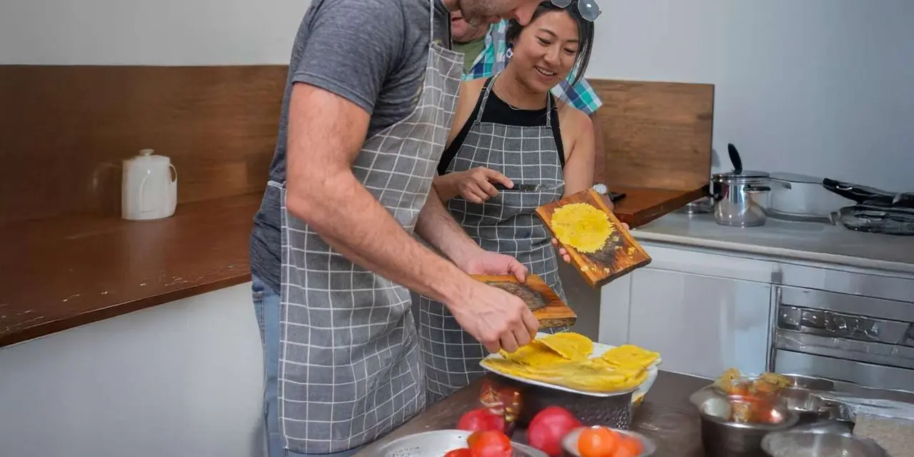 A man in an apron plating food at a kitchen counter while a woman looks on