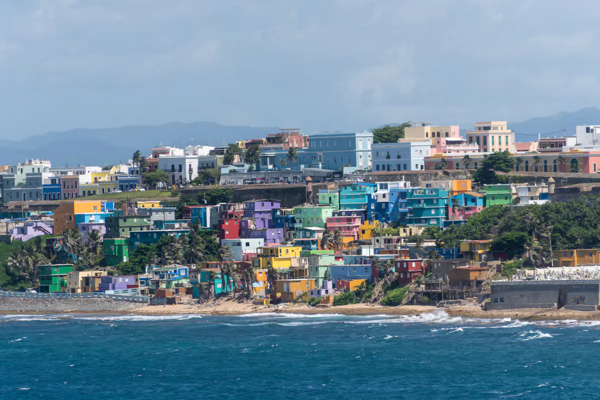 The brightly painted houses of La Perla stacked along Old San Juan's waterfront below the city walls, seen from the sea with blue water in front
