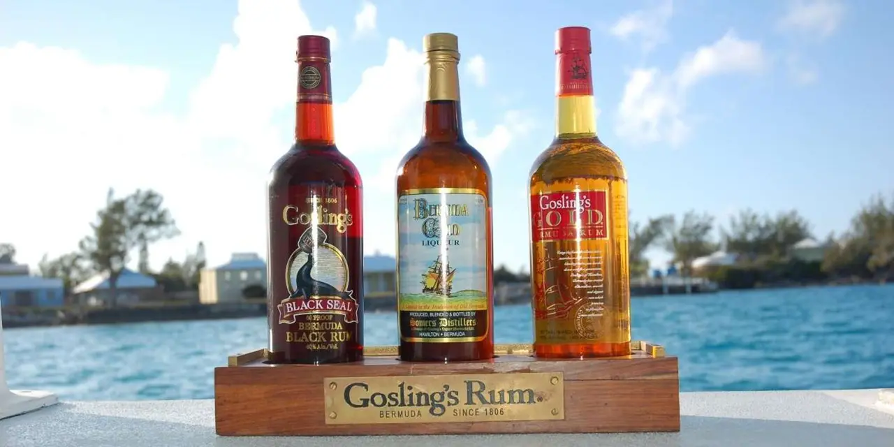 Three bottles of Gosling's rum lined up on a tray on a boat deck above the water