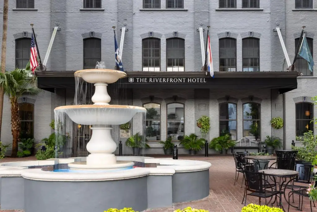 The Riverfront Hotel's grey-brick facade with flags over the entrance and a tiered fountain in the brick courtyard in front