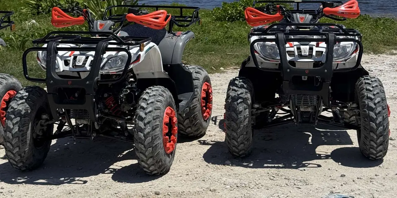 Two white-and-black ATVs with red wheel hubs and hand guards parked side by side on a gravel beach path beside the water