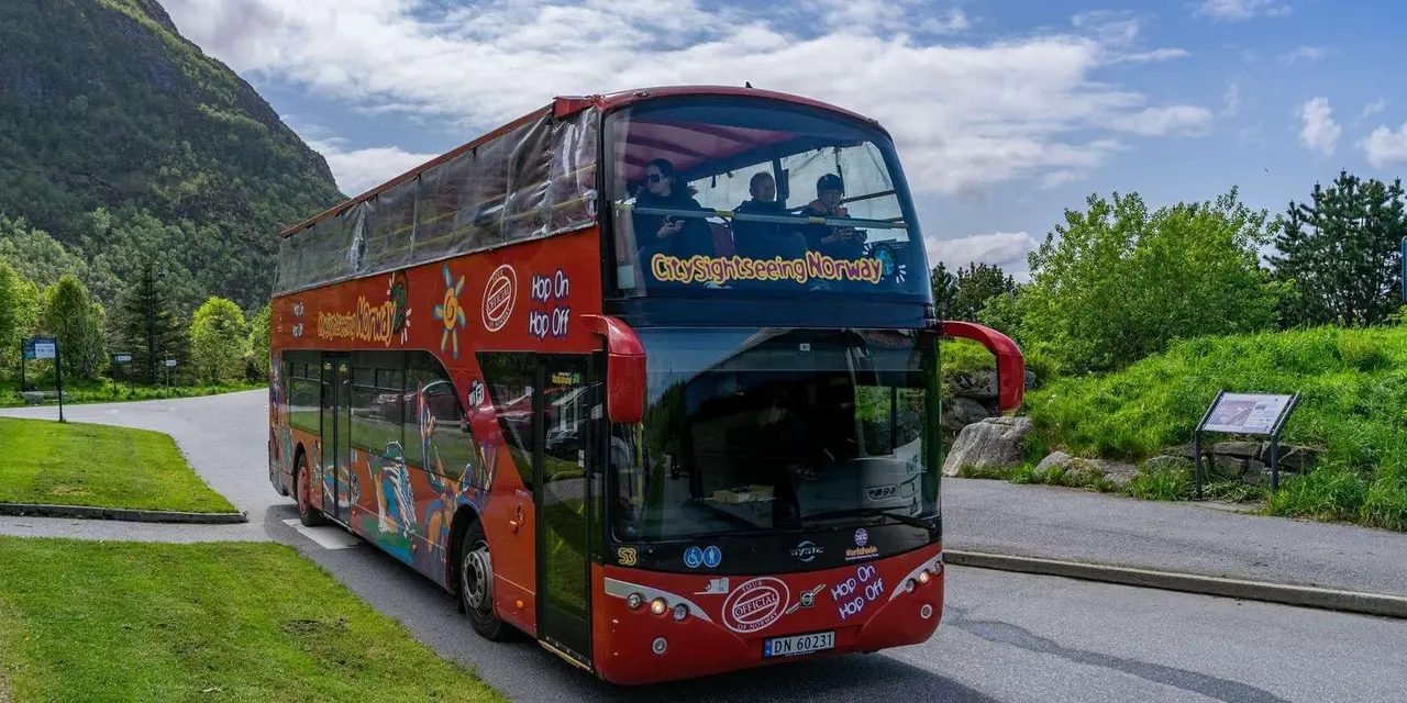 A red open-top City Sightseeing double-decker bus parked on a roadside below a green mountain