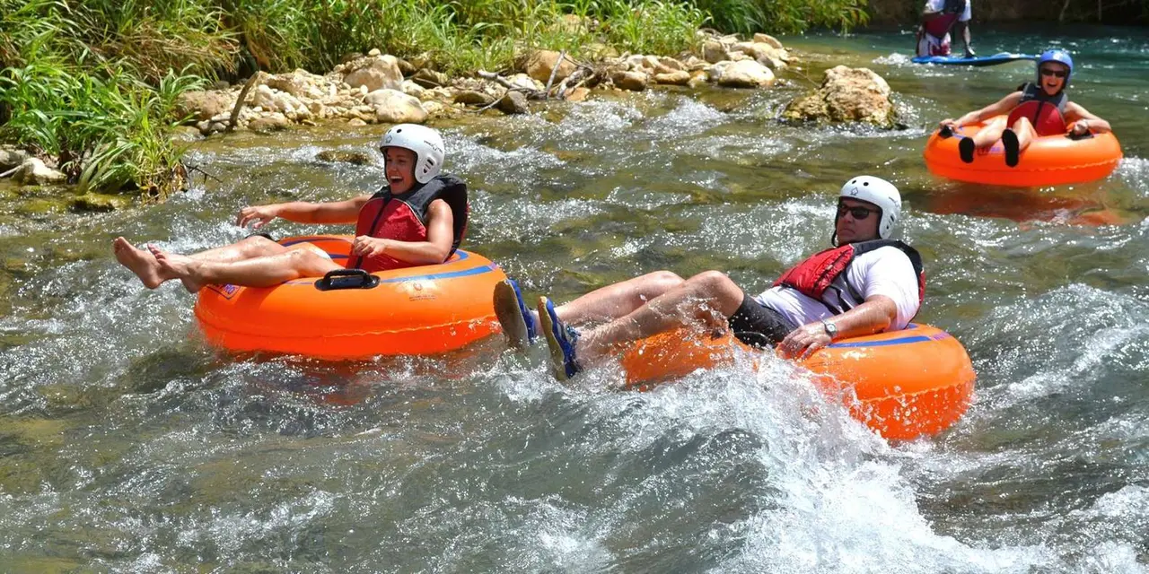 People in helmets riding orange inner tubes down a rocky jungle river