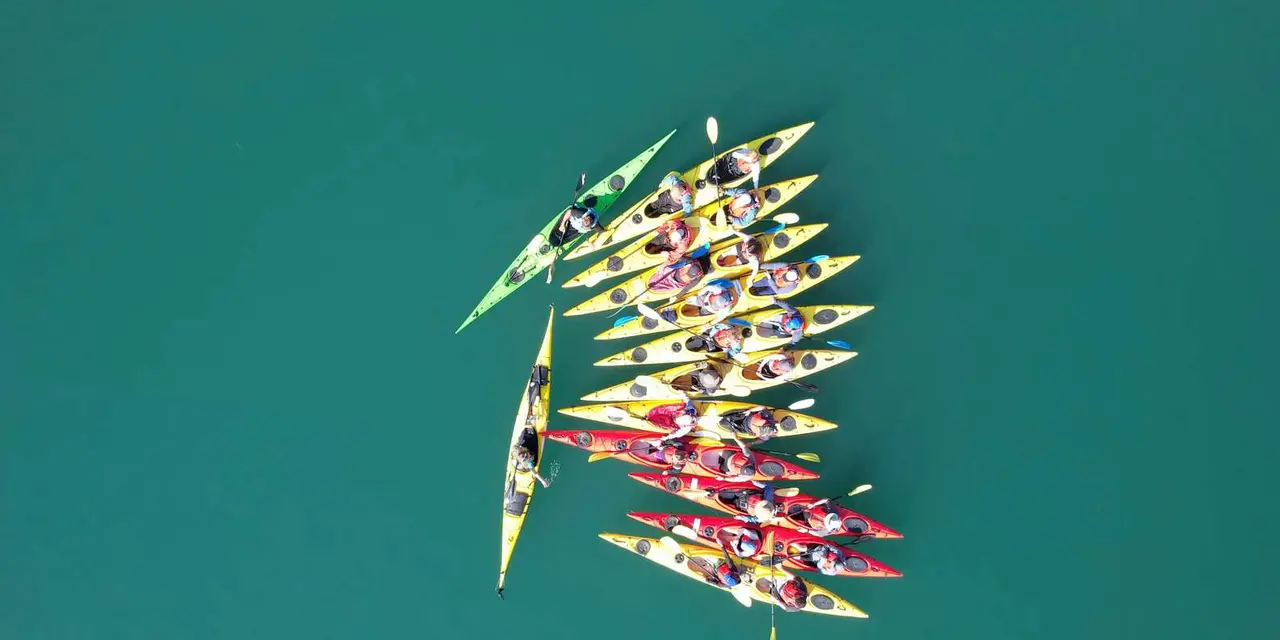 An overhead view of yellow, green and red kayaks grouped on teal fjord water