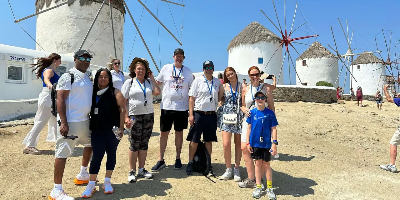 A tour group posing on a sandy rise in front of two white windmills under a blue sky