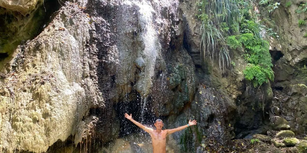 A person with arms out beneath a waterfall on a rock face